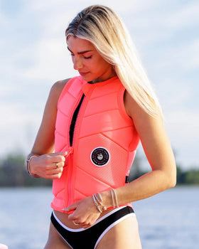 Blonde woman zipping up a Follow impact vest before wakesurfing, preparing for a ride behind the boat.