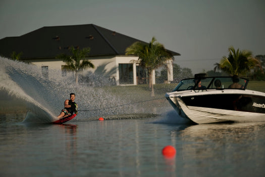 Waterskier carving around a buoy on a Radar slalom ski while being pulled by a boat through the course.