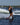 Progressing girl wakeboarder cruising with one hand off the handle and waving on the 2026 Ronix Krush 125cm wakeboard package.