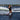 Progressing girl wakeboarder cruising with one hand off the handle and waving on the 2026 Ronix Krush 125cm wakeboard package.