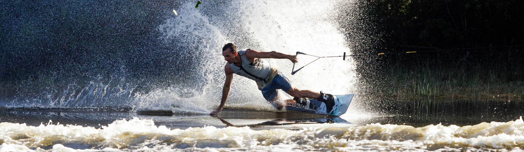 Man tilting and touching the water while riding a wakeboard