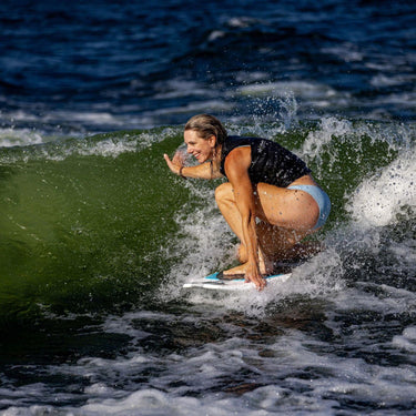 Pro rider Stacia Bank kneeling on her signature Phase 5 Swell Wakesurfer in the sweet spot of the wake.
