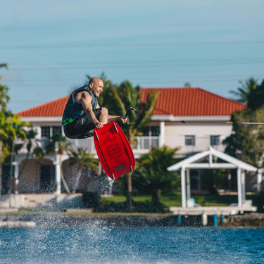 Rider launching a clean tail grab wake-to-wake jump on the complete 2026 Ronix District wakeboard with Divide Boot wakeboard package.