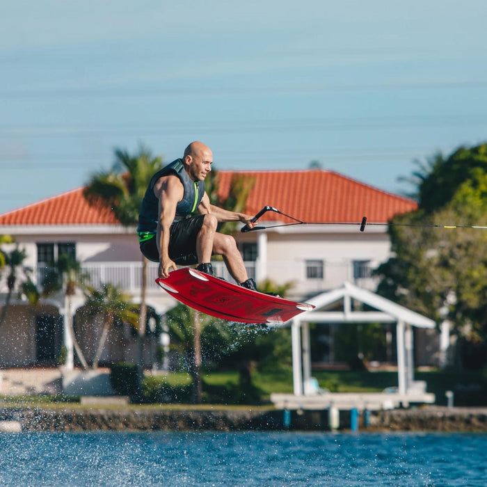 Wakeboarder performing a wake-to-wake jump with a stylish tail grab on the Ronix District.