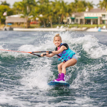 Young girl grom wakeboarder smiling and learning how to carve outside the wake on the complete 2026 Ronix August 120cm wakeboard package.