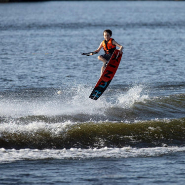 Young grom wakeboarder confidently executing a tailgrab in the air on the complete 2026 Ronix Kid's Vault wakeboard package.