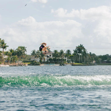 Pro rider Kira Lewis clearing the wake with a massive, high-flying air on her 2026 Ronix Quarter 'til Midnight wakeboard setup.
