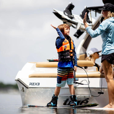 Young grom sitting on the swim step, strapped into the 2026 Ronix Vision board and boot package, ready to ride.