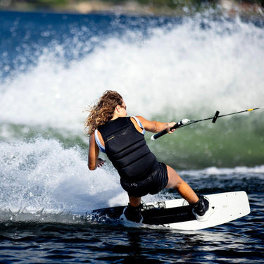 Female rider carving on the Ronix Quarter 'til Midnight board with Halo open-toe boots, showing a high-performance women's boat setup.