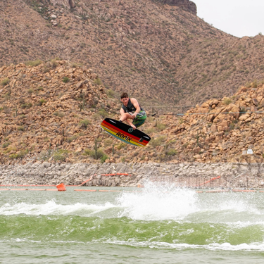 Wakeboarder executing a toeside grab wake-to-wake jump on the 2027 Ronix Parks wakeboard setup.